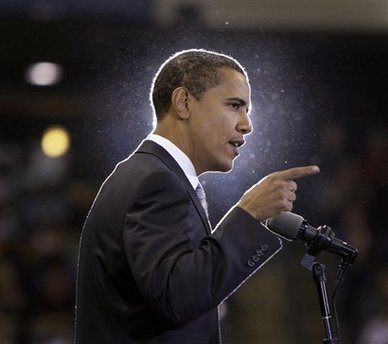a photo of Barack Obama standing at a podium. The spotlight behind him gives a halo effect